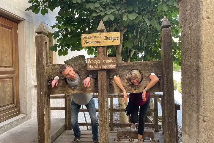 Visitors pose at the Rothenburg Plönlein pillory for a fun stop on the self-guided scavenger hunt tour