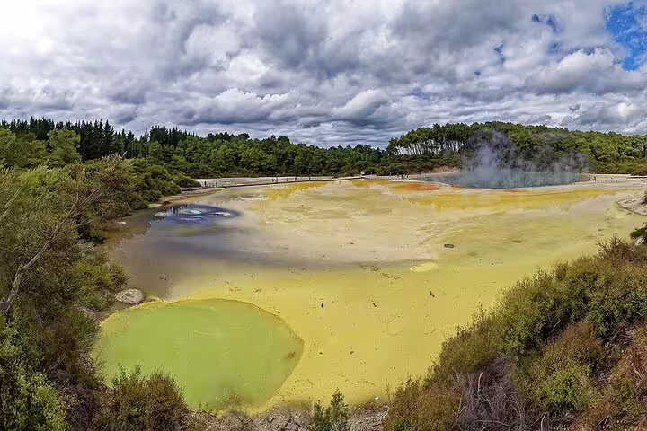 Vibrant geothermal landscape of Rotorua with colorful mineral pools and lush greenery under a dramatic sky.