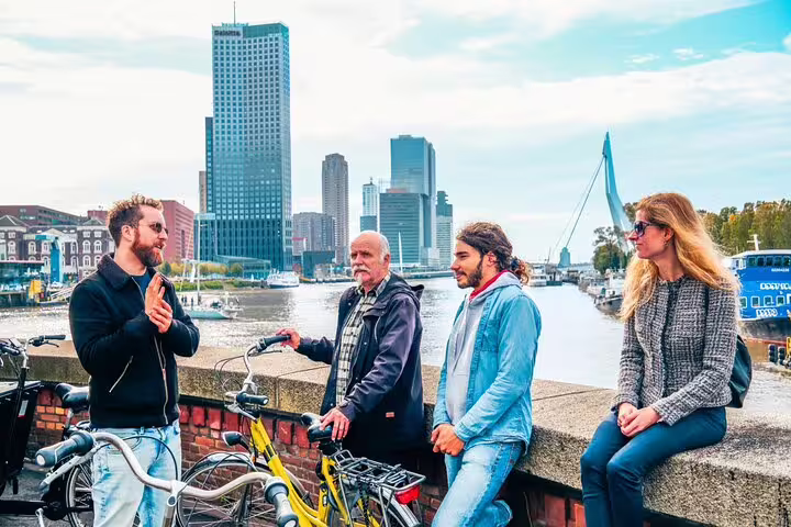 Local guide briefs cyclists by the Erasmus Bridge skyline on a classic Rotterdam highlights bike tour