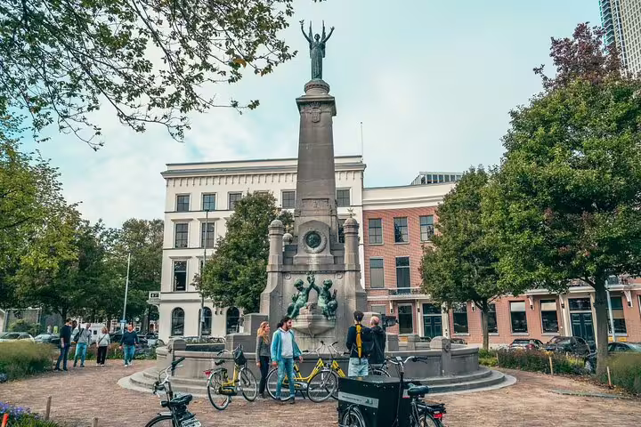 Cyclists pause by Rotterdam’s historic monument on a guided highlights bike tour with a local guide