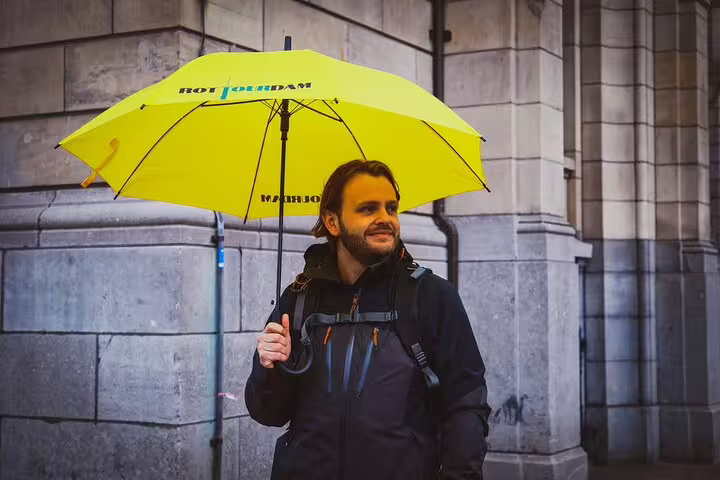 Dutch local guide with yellow umbrella on Rotterdam walking tour, sharing highlights and hidden gems in rain