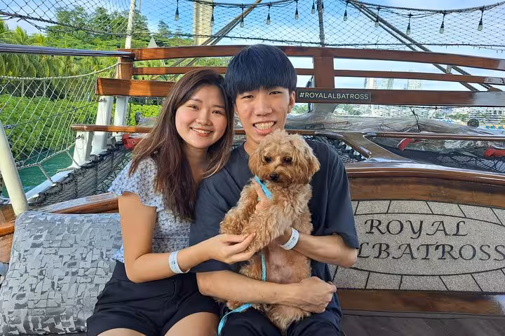 Smiling couple with dog on the Royal Albatross, savoring a sunset sail with scenic views and dinner onboard.