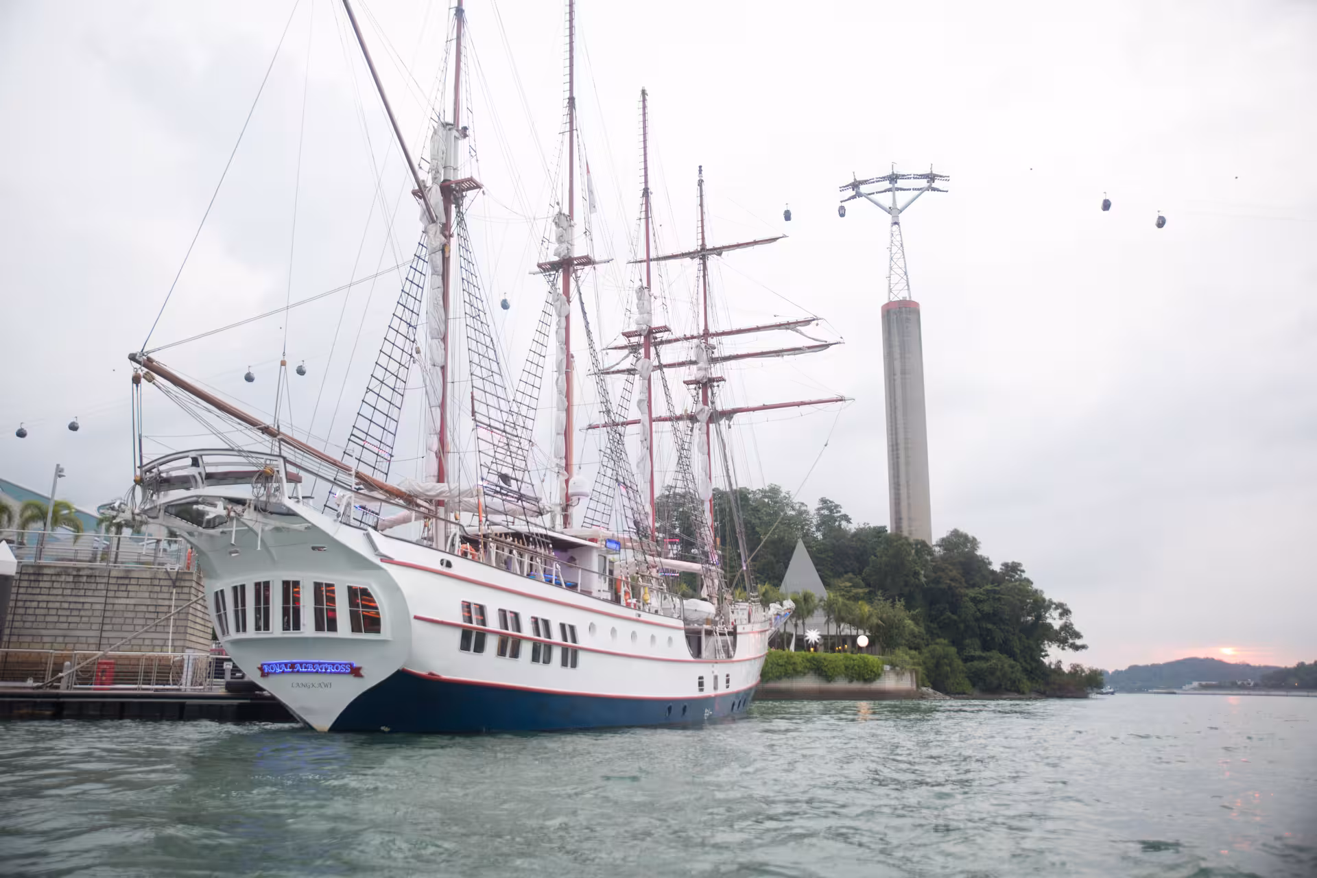 The Royal Albatross docked at harbor, ready for a sunset sail with a scenic backdrop and cable cars overhead.