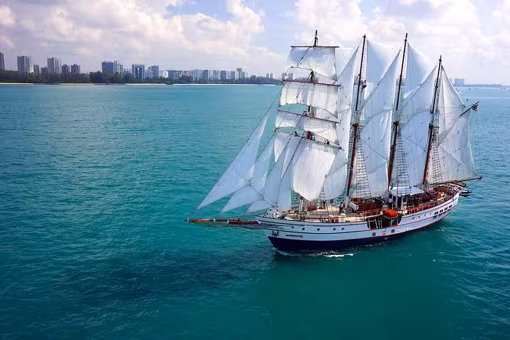 Majestic tall ship sailing on clear blue waters with a city skyline in the background.