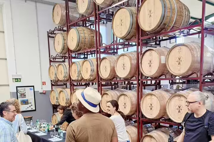 Tour group exploring a rum distillery with stacked barrels, part of the Sunny Southwest Rum and Lighthouse Discovery tour.