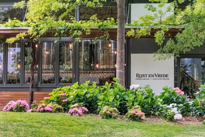 Charming exterior of Rust en Vrede tasting room surrounded by lush greenery and blooming flowers in Stellenbosch.