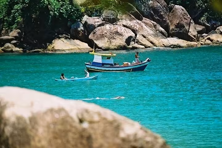 A boat and kayakers explore the vibrant blue waters near rocky shores on the Saco Bravo Waterfall adventure tour.