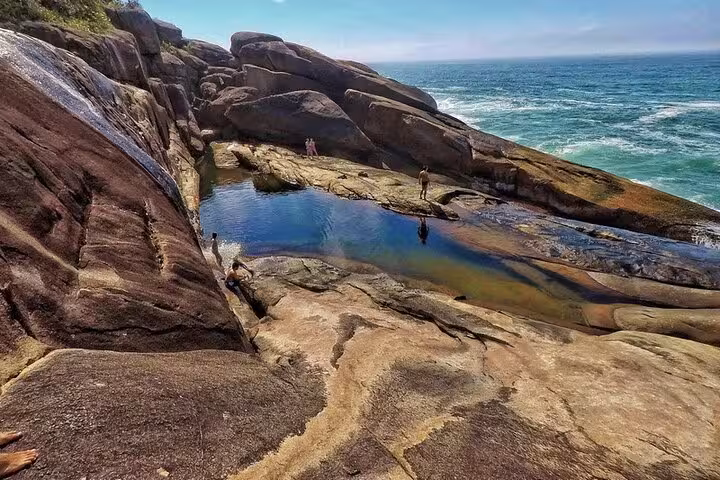 Visitors enjoy a natural pool on rocky formations by the sea at Saco Bravo Waterfall, Paraty tours adventure spot.