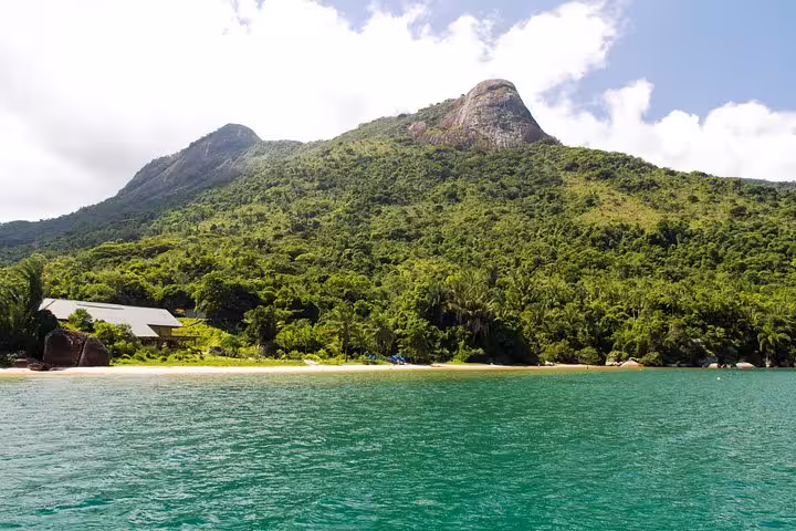 Lush green hills and serene beach at Saco Mamanguá Fjord, perfect for a half-day tour exploring idyllic Brazil.