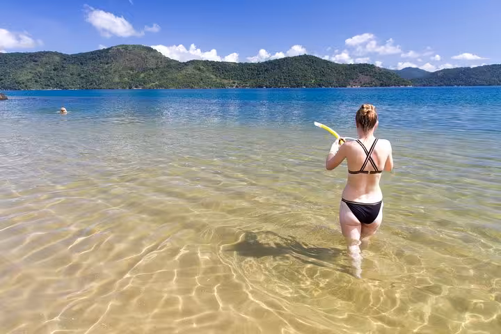 Tourist snorkels in clear waters of Saco Mamanguá Fjord, surrounded by lush green hills and serene beaches.