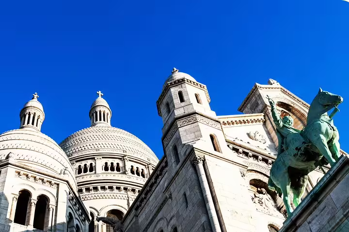 Sacré-Cœur domes and rooftop statue against blue sky on a Montmartre highlights self-guided tour in Paris