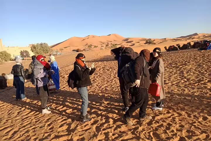 Travelers in Sahara dunes at Merzouga camp stop on 3 days desert tour from Fes to Marrakech, Morocco