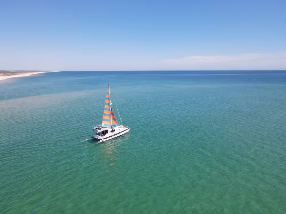 Sailing catamaran with striped sails cruising across the Algarve Blue Lagoon on a half-day catamaran trip
