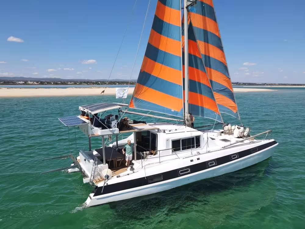 Sail catamaran cruising Blue Lagoon with striped sails over turquoise sea, half-day sailing and lagoon swim stop