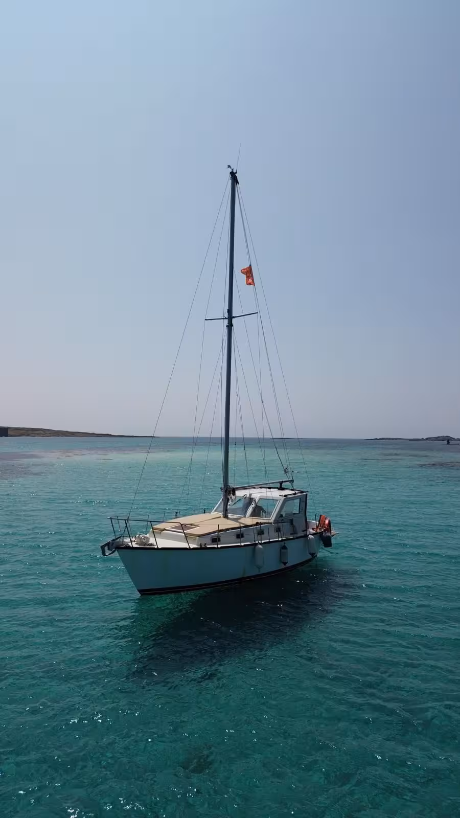 A sailboat floats serenely on turquoise waters under a clear sky in Asinara National Park, perfect for a sailing trip.