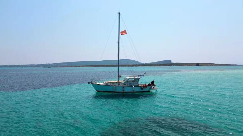 Sailboat gliding on turquoise waters in Asinara National Park, showcasing serene views and a perfect sailing adventure.