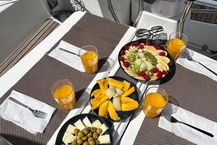 Luxurious sailboat dining setup with fresh fruit platters, cheese, olives, and orange juice on a private Ibiza and Formentera day trip.