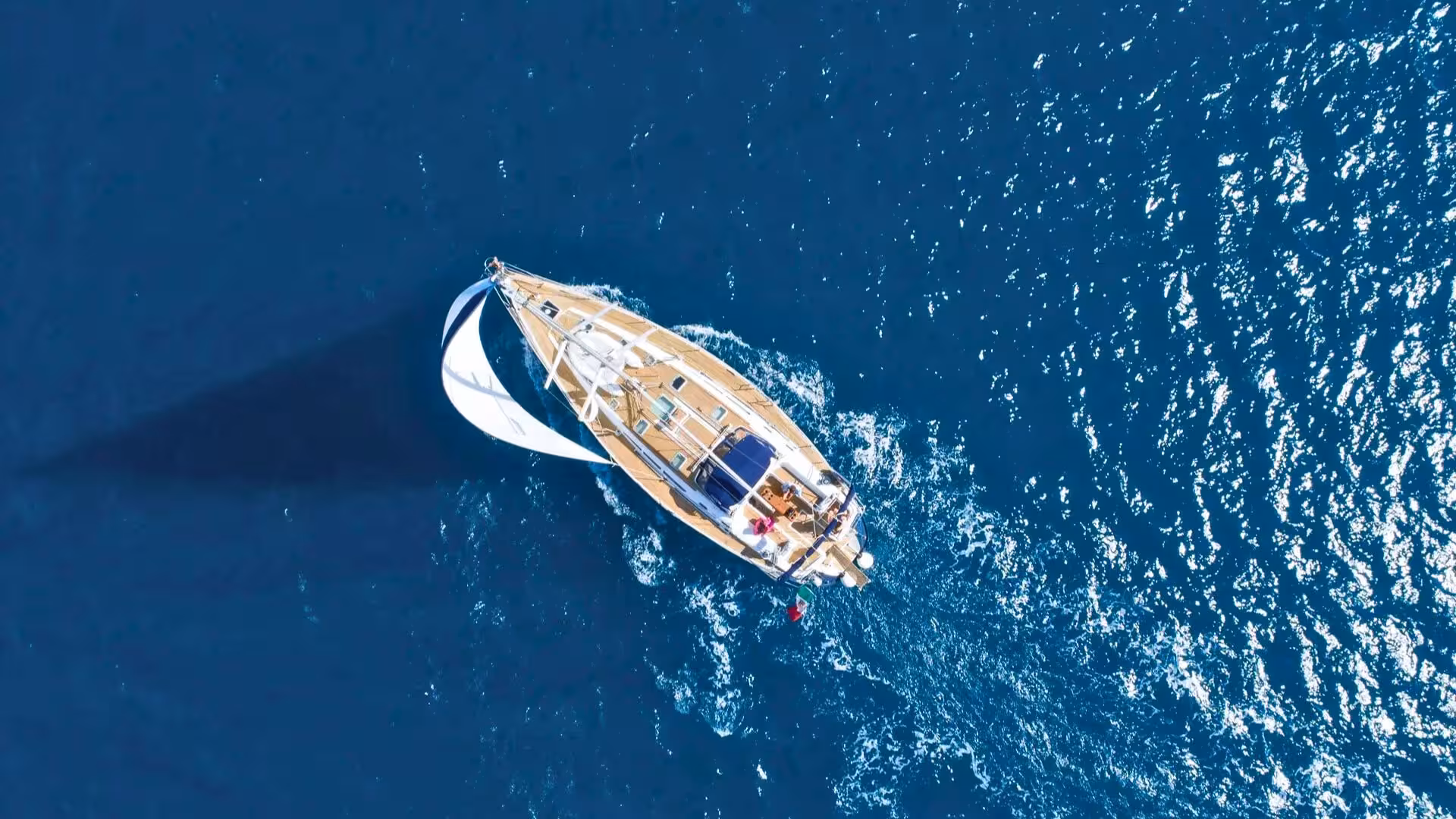 Aerial view of a sailboat cruising the deep blue waters of the Gulf of Orosei, showcasing a serene sailing experience.