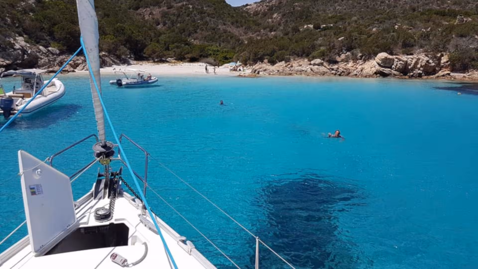 Sailboat anchored in crystal-clear waters of La Maddalena Archipelago, surrounded by scenic rocky coastline.