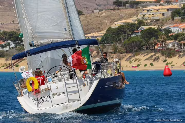 Sailboat cruising along Madeira's scenic south coast with passengers enjoying the ocean view, vibrant landscape, and sunny weather.