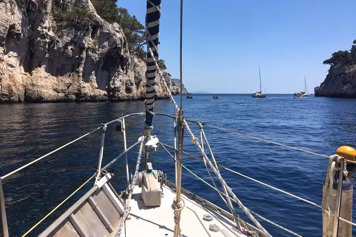 Sailboat bow entering Marseille Calanques, limestone cliffs and calm Mediterranean water on a scenic sailing cruise