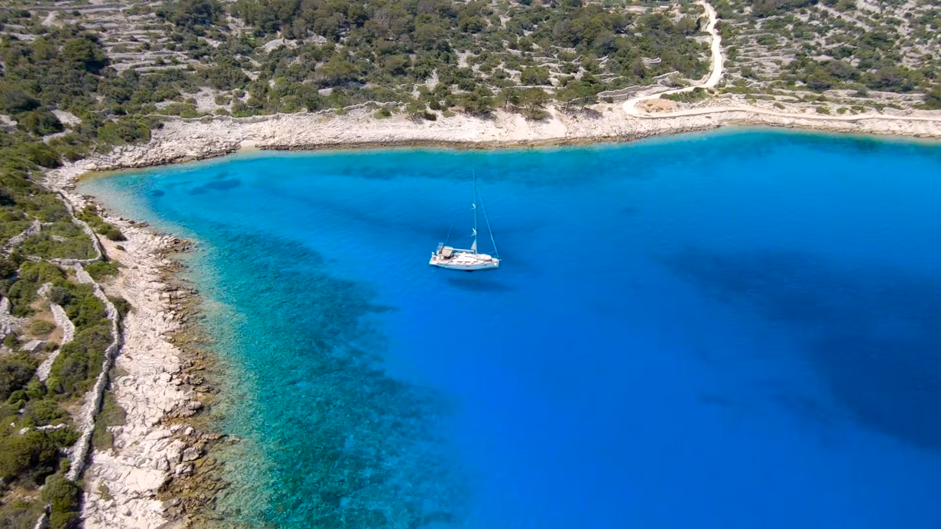 Sailboat anchored in a calm blue bay by rocky coast, Archipelago Adventure yacht cruise and swim stop