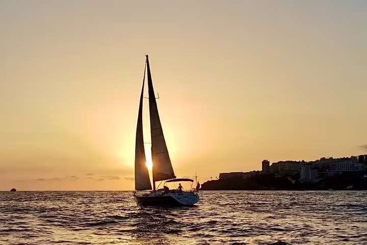 Sailboat cruising at sunset in Madeira with golden skies, perfect for private sunrise, sunset, and moonlight sailing tours.