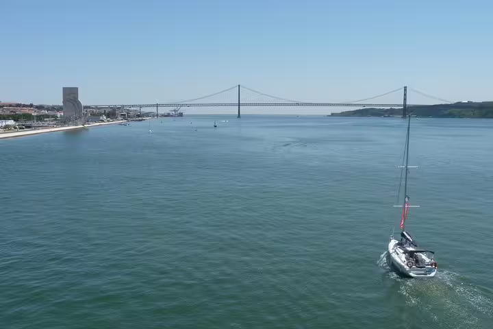 Sailboat navigating the Tagus River near the iconic 25 de Abril Bridge in Lisbon.