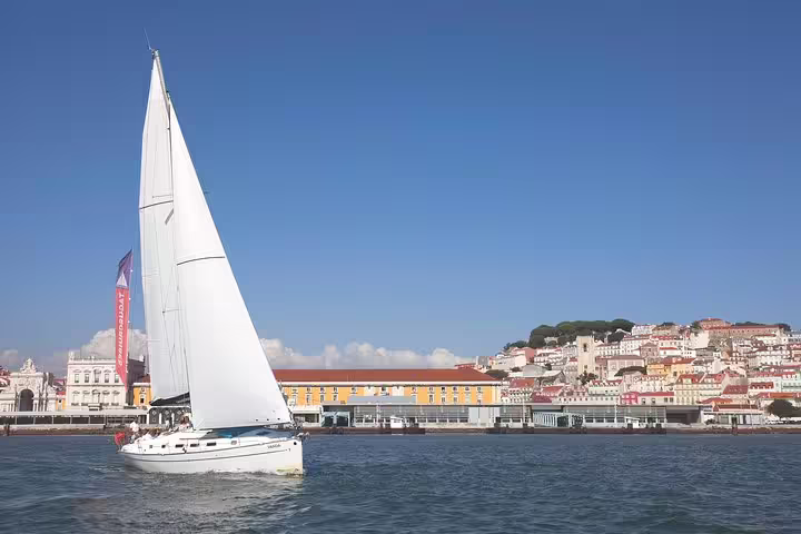 Sailboat gliding on Tagus River with Lisbon's historic architecture in the background under a clear blue sky.
