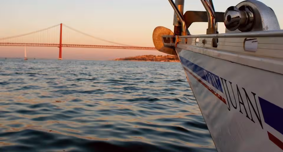 Sailboat bow cruising the Tagus at sunset with 25 de Abril Bridge in view on Cultural Sail Tour Lisbon