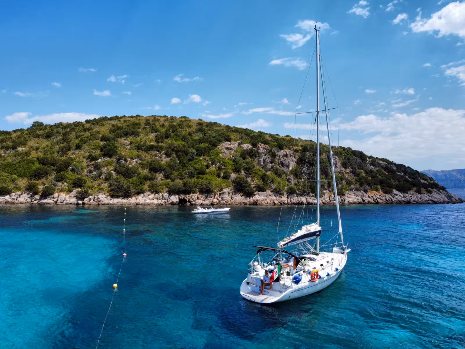 Sailboat anchored in turquoise waters near a lush island on the Tavolara and Cala Moresca tour.