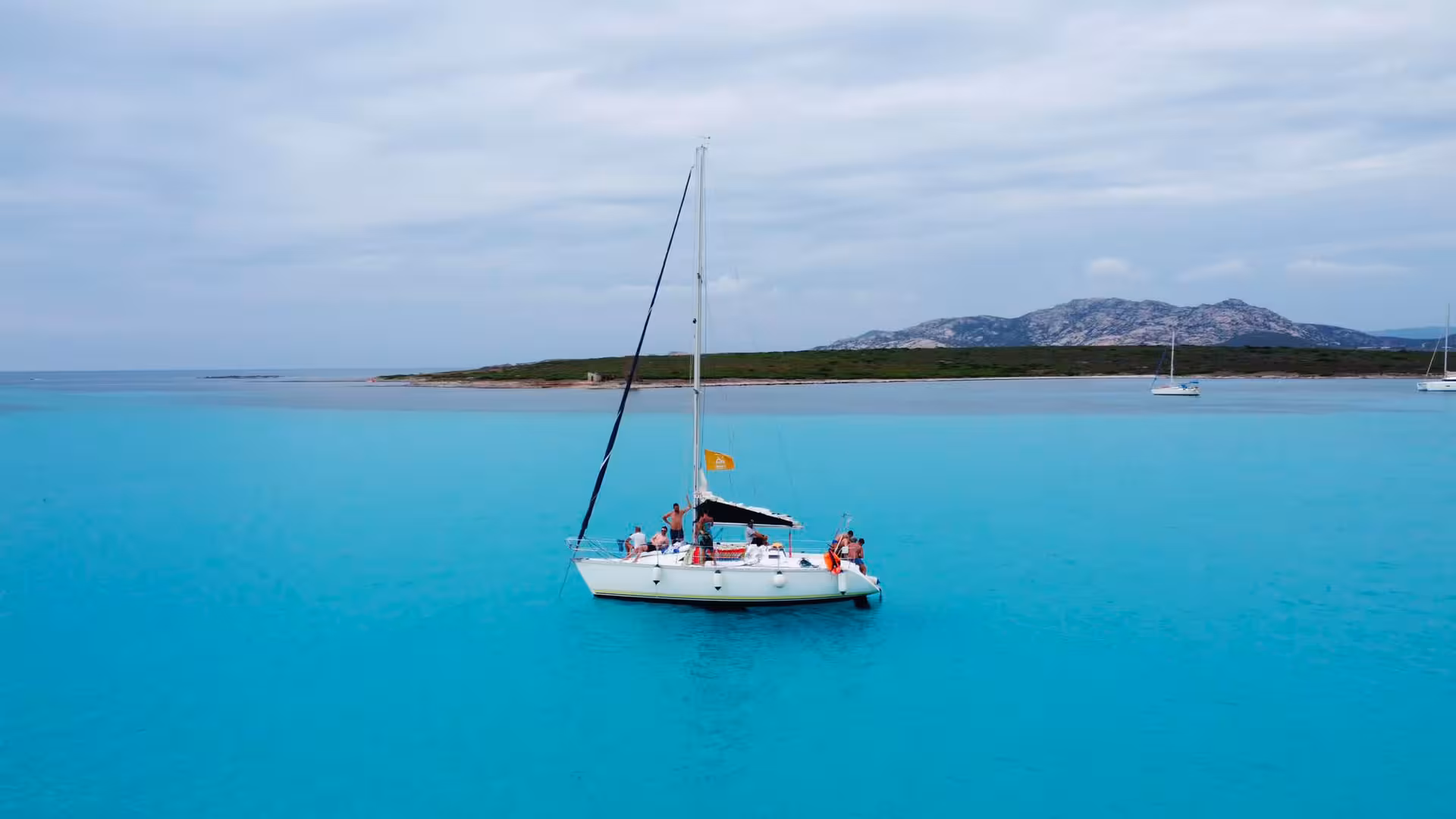 Aerial view of a sailboat cruising on clear blue waters with Asinara Island in the background.
