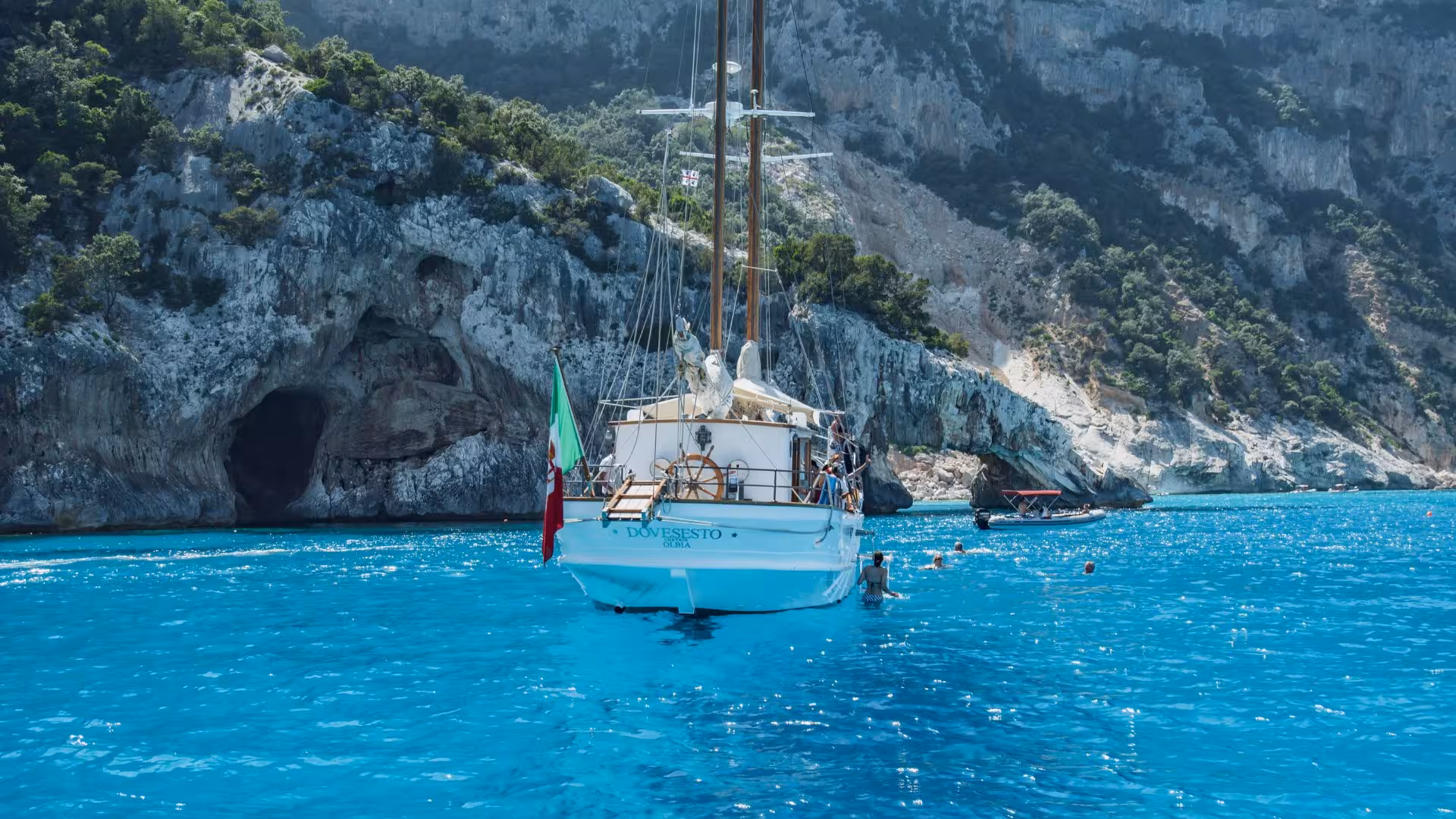 Sailboat anchored near rocky cliffs in the Gulf of Orosei, with swimmers enjoying the turquoise waters around Cala Gonone.