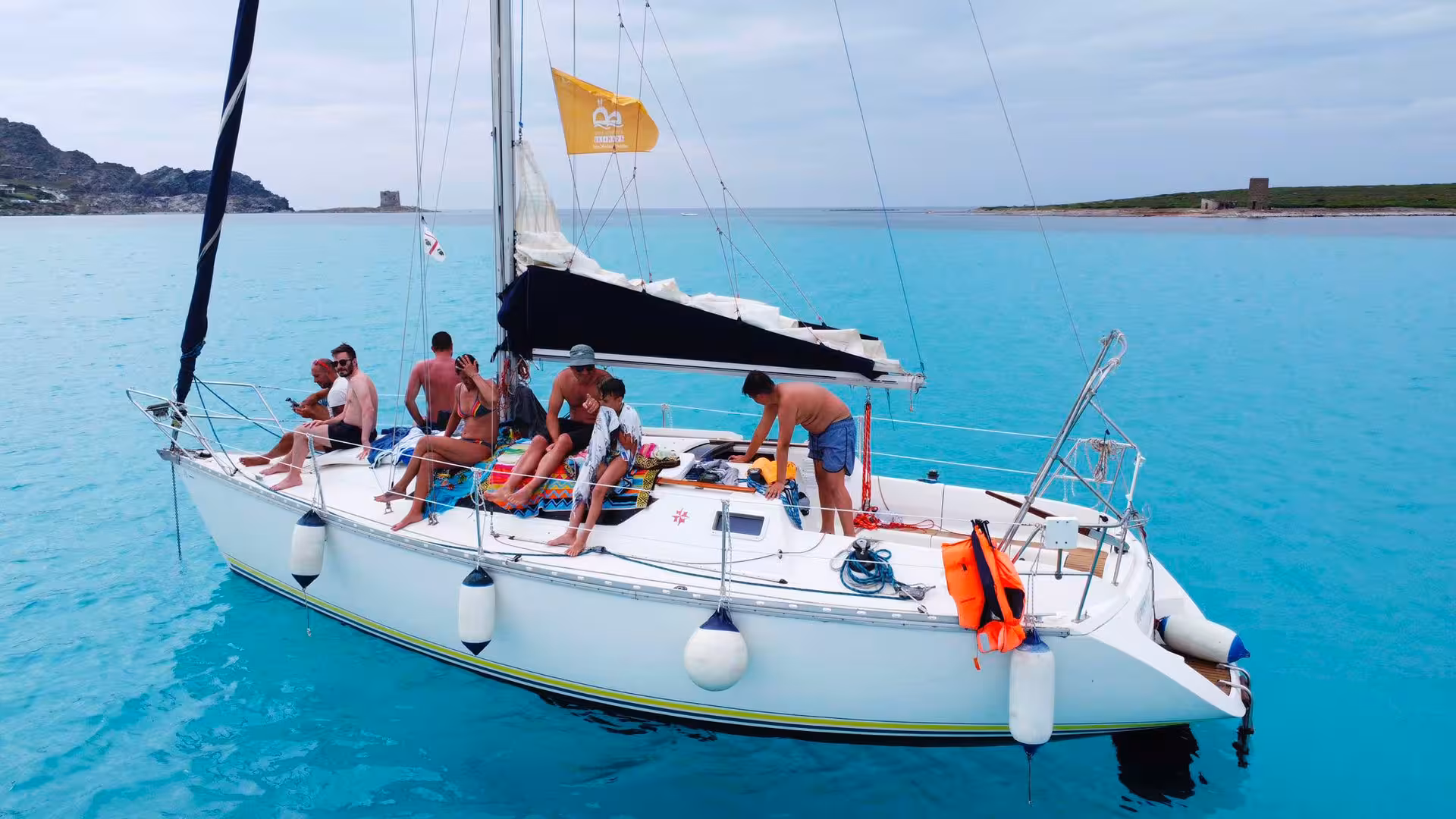 Sailboat with tourists enjoying a sunny day on turquoise waters near Stintino during Asinara tour.