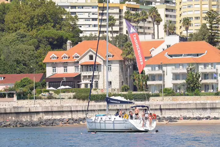 Sailboat with tourists near Oeiras beach, showcasing seaside architecture and lush greenery on a sunny day.