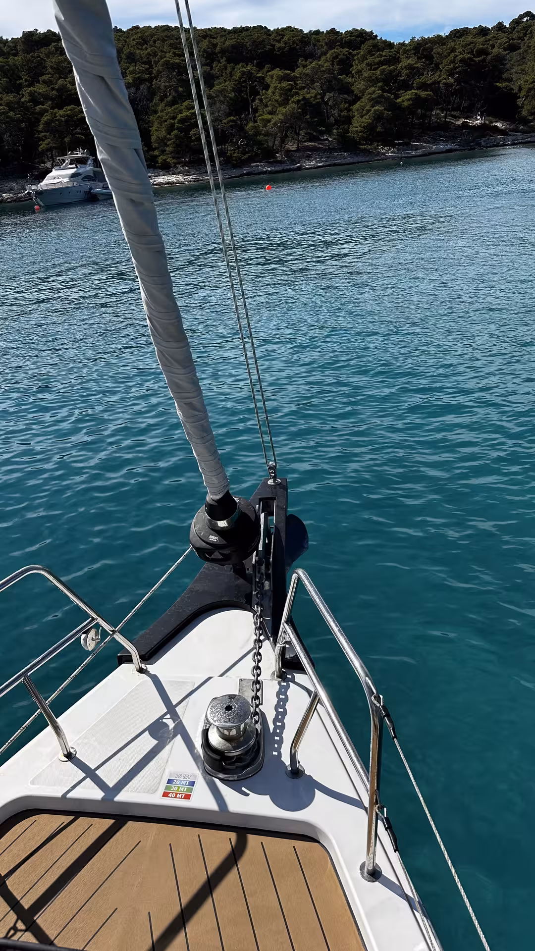 Sailboat bow anchored in turquoise bay by pine-covered coastline, beginner sailing “Zero to hero” training day