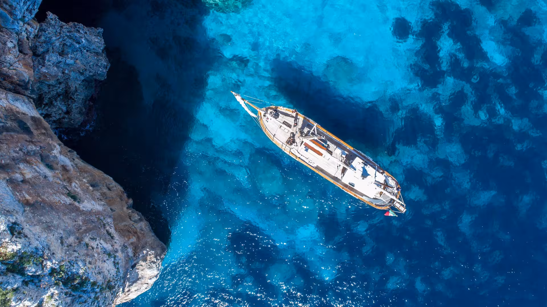Aerial view of a sailing boat navigating the vibrant blue waters of the Gulf of Orosei near Cala Gonone.
