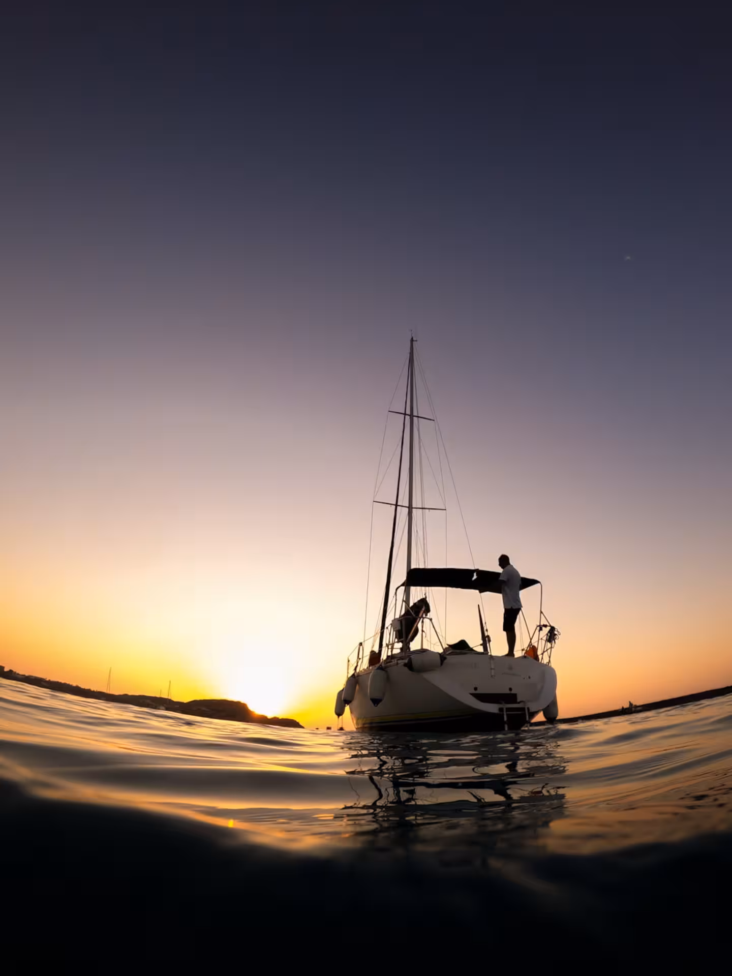 Sailing boat at sunset in Stintino, Sardinia, offering a serene view of Pelosa Beach with a golden horizon.
