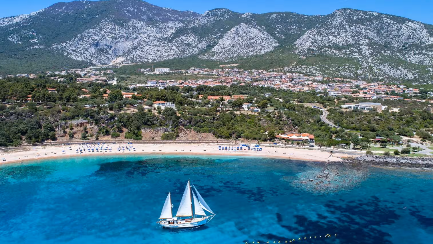 Sailing boat in clear blue waters with a backdrop of Cala Gonone's beaches and lush mountainous landscape.