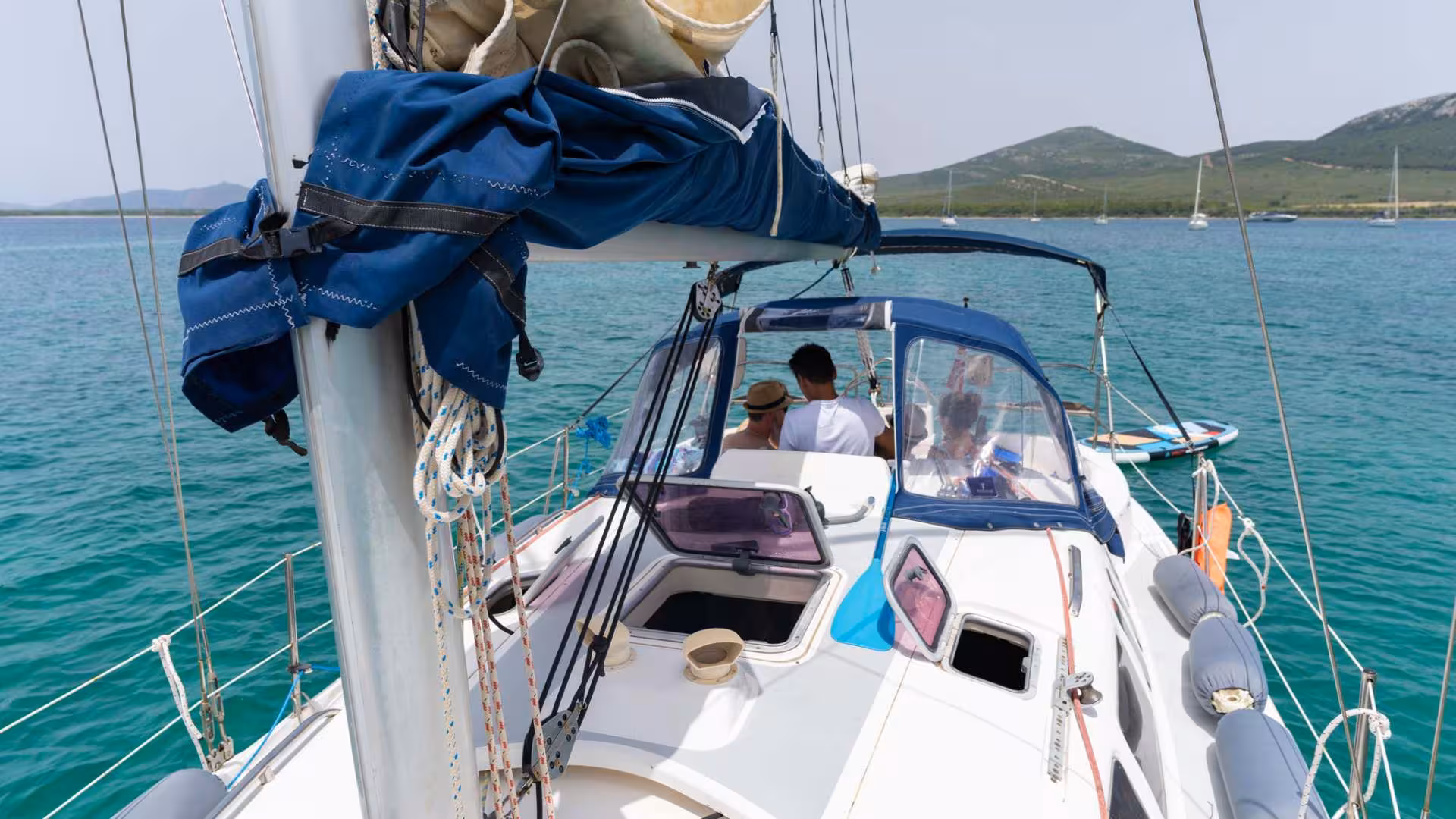 Group of people enjoying a sailing experience in Porto Conte Park, Alghero, aboard a yacht on turquoise waters.