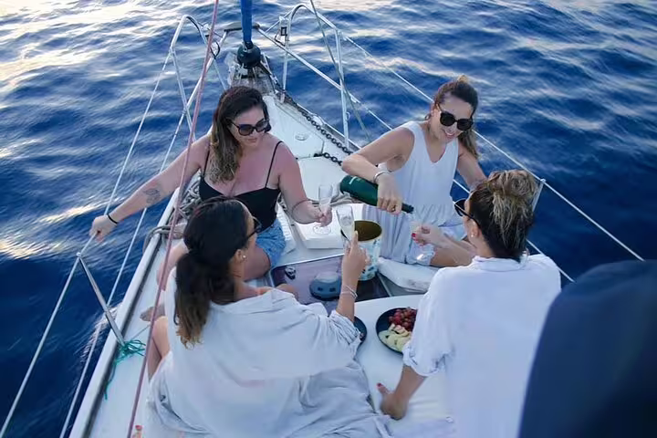 Group of friends enjoying a luxurious sailing trip with drinks and snacks on a yacht in the clear waters of Ibiza and Formentera.