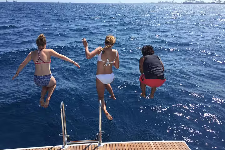 Three people jumping off a boat into the ocean during a sailing trip with drinks, snacks, and swimming time included.