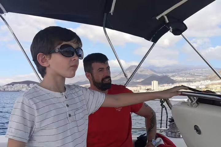 Father and son enjoying a sailing yacht adventure with stunning coastal views on a private charter.