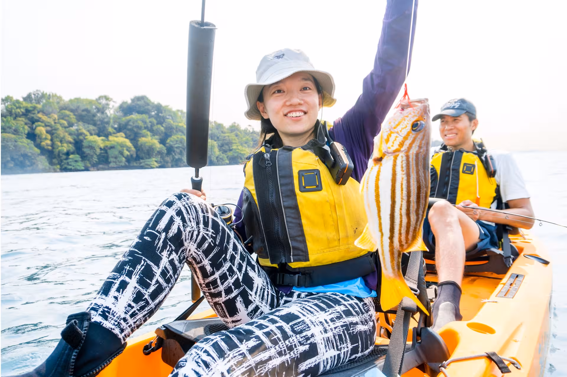 Smiling kayakers on Saint John Island tour holding a colorful fish amidst scenic waters.