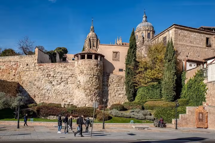 Historic stone walls and towers of Salamanca with lush greenery on a sunny day, perfect for a guided city walk tour.