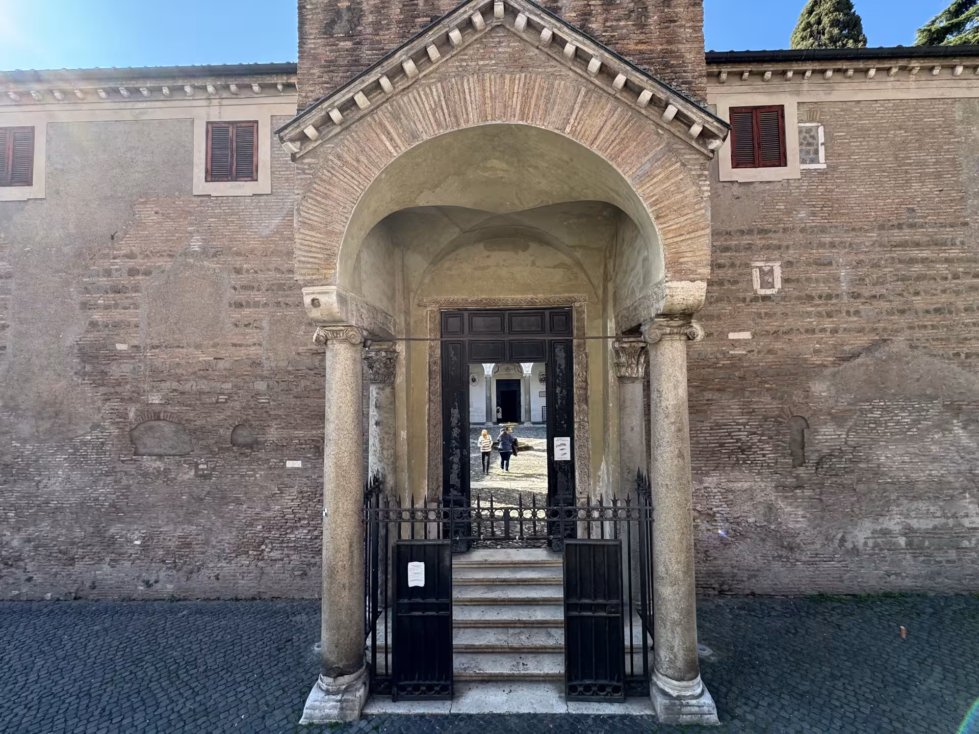 Entrance courtyard of San Clemente Basilica in Rome with ancient brick façade and arched doorway leading to underground tour