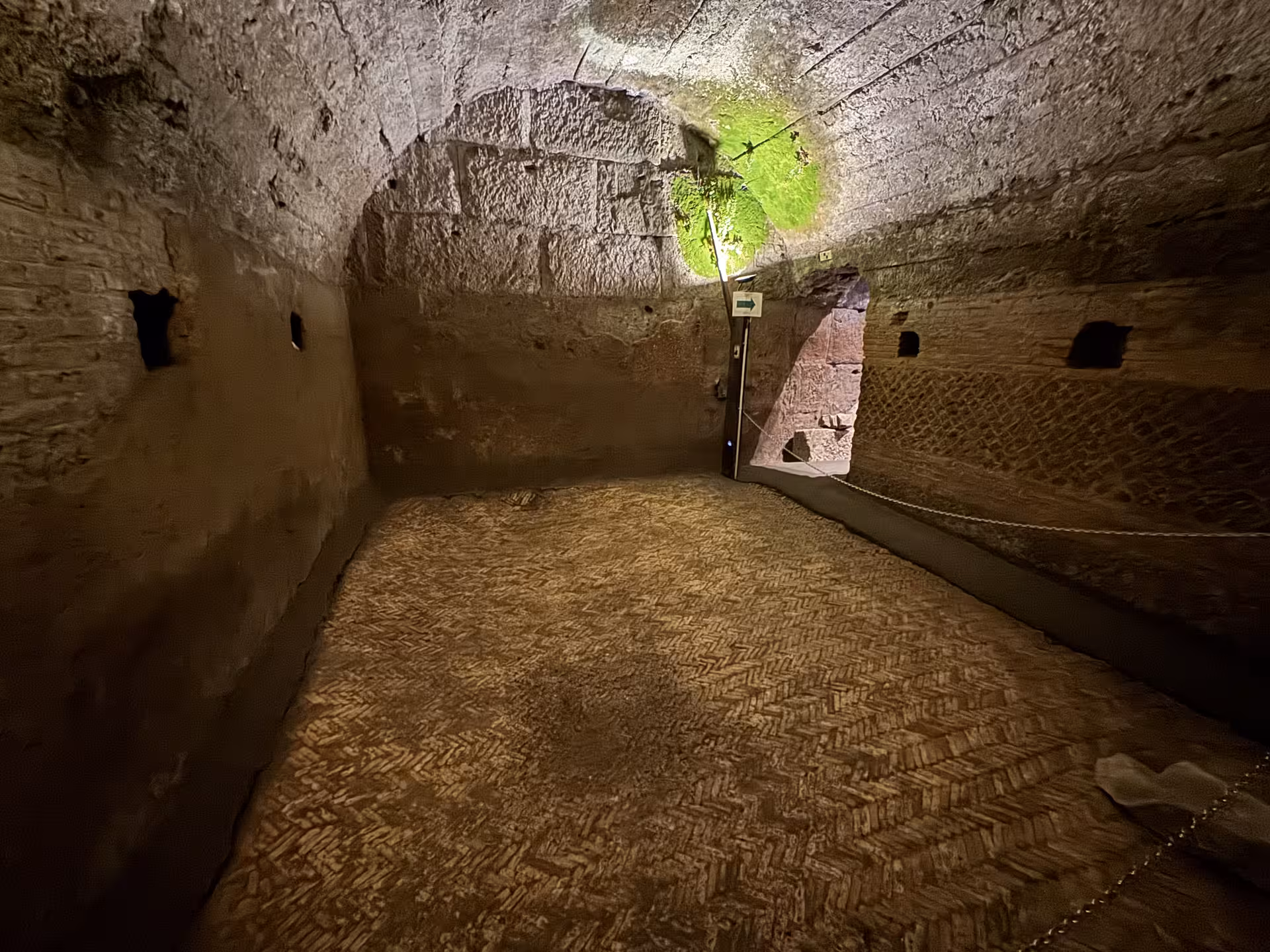 Dimly lit underground chamber with ancient brick walls and herringbone floor beneath San Clemente Basilica in Rome, Italy