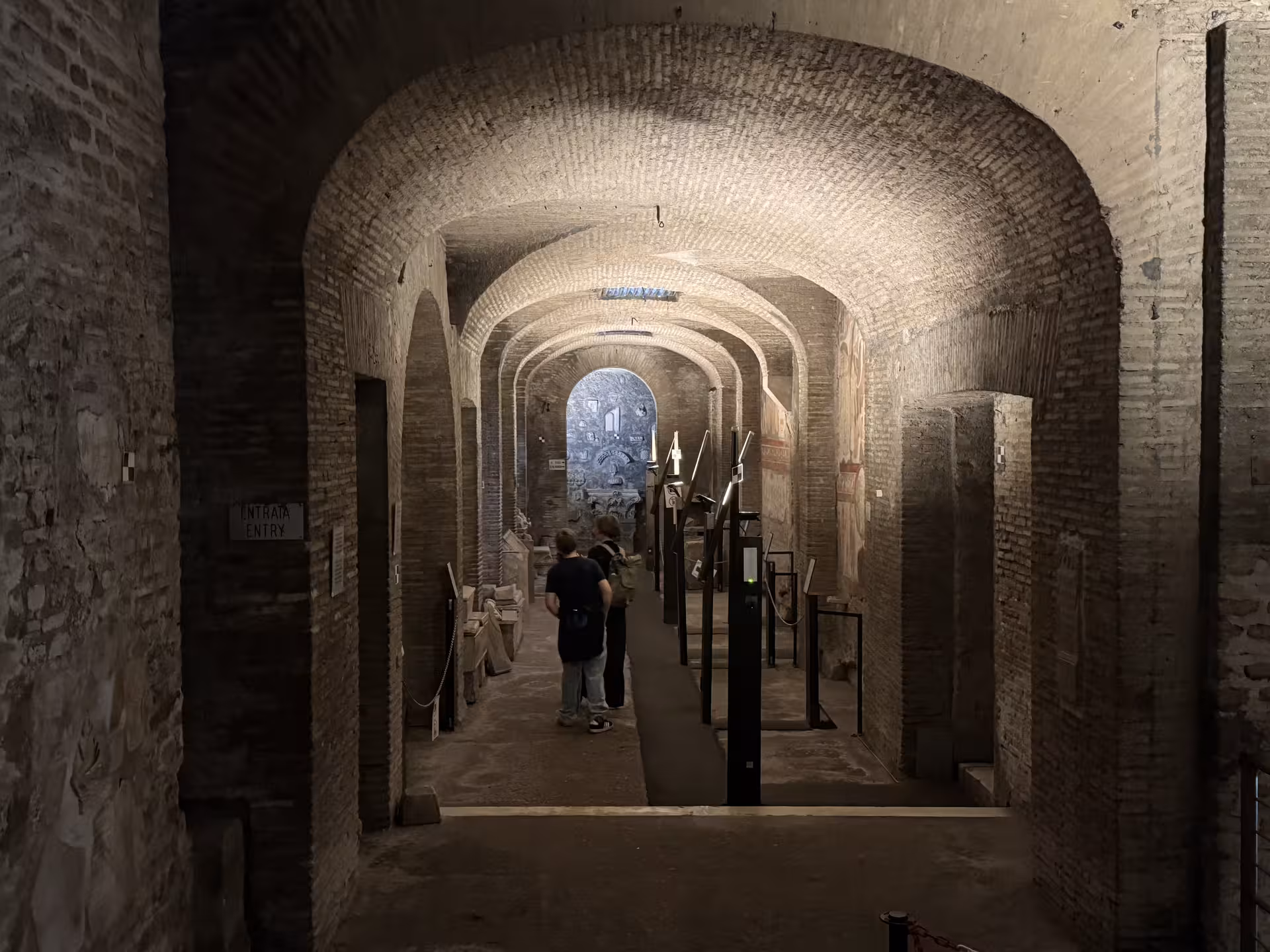 Visitors explore the dim brick corridors and ancient frescoes of the underground levels of San Clemente Basilica in Rome