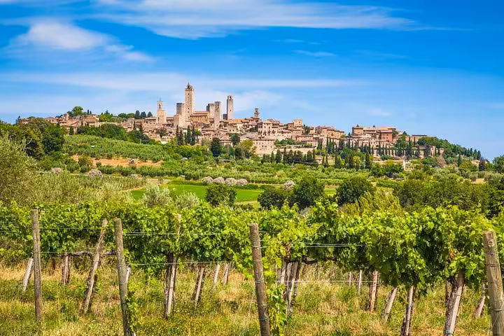 Scenic view of San Gimignano's medieval towers behind lush vineyards under a bright blue sky in Tuscany, Italy.