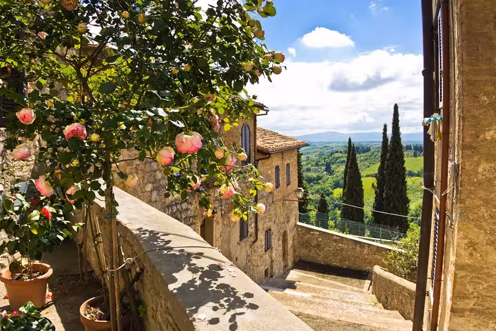 Charming view of San Gimignano's rustic stone buildings and lush Tuscan countryside on a sunny day.